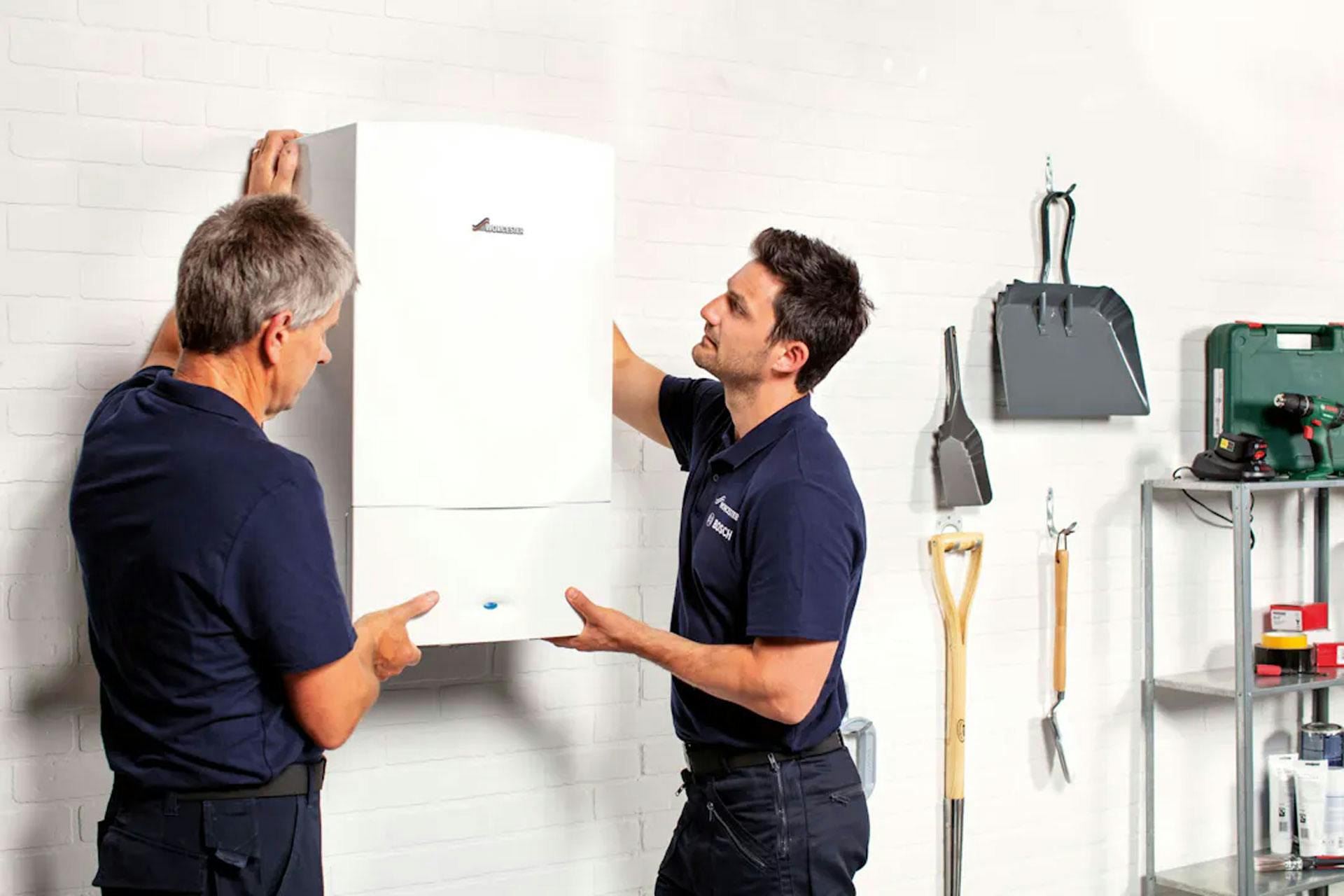 Two men installing a wall-mounted boiler in a utilities room