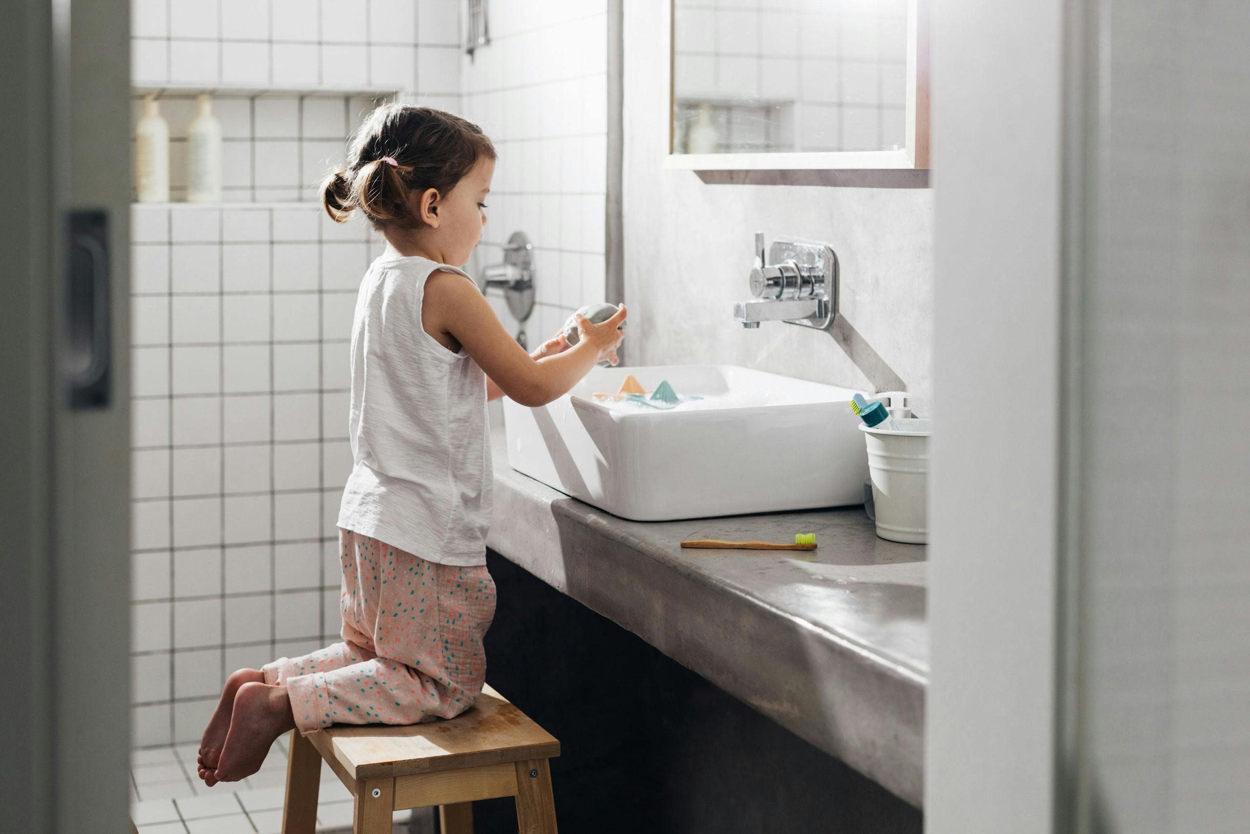 Young girl kneeling on a stool while washing her hands in the sink