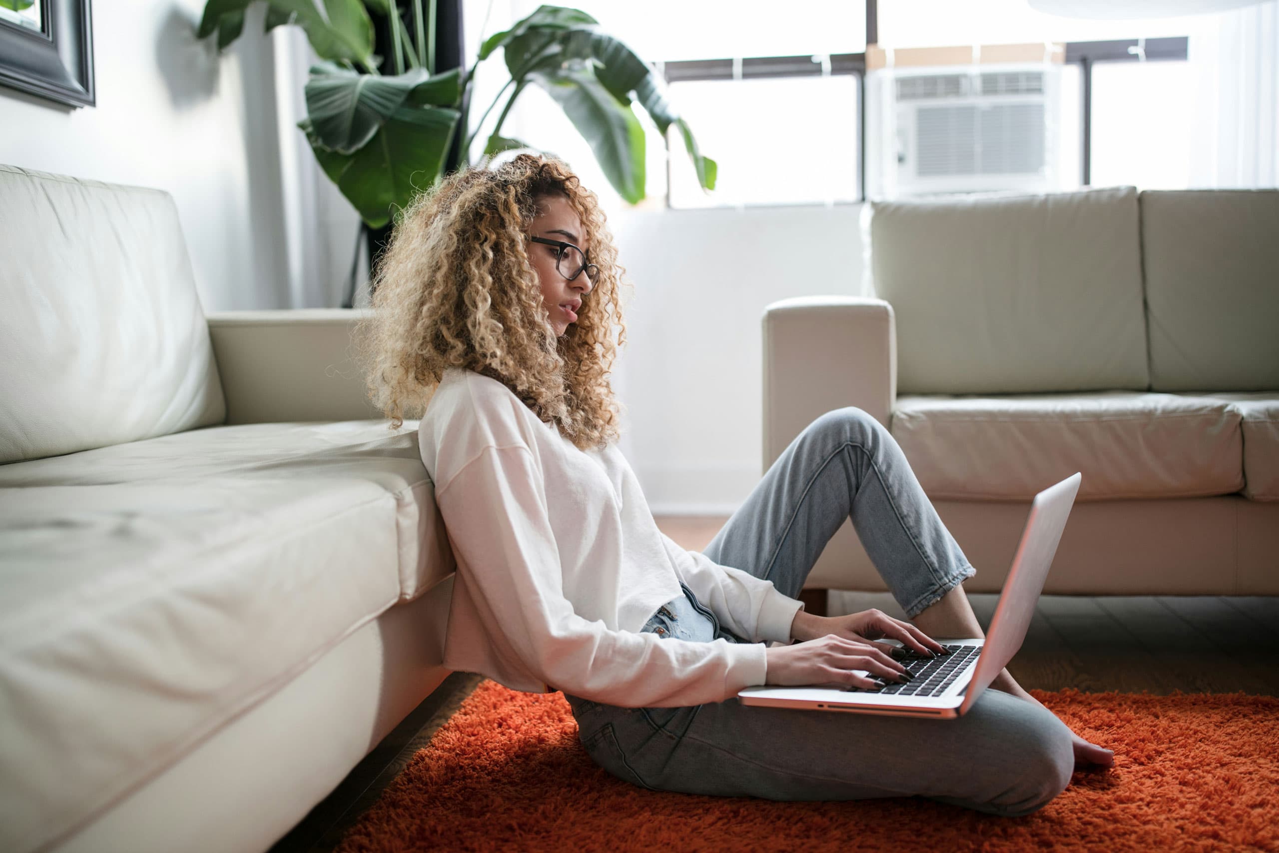 A woman sat on the floor in front of her sofa, while searching for a solar panel kit on a laptop.