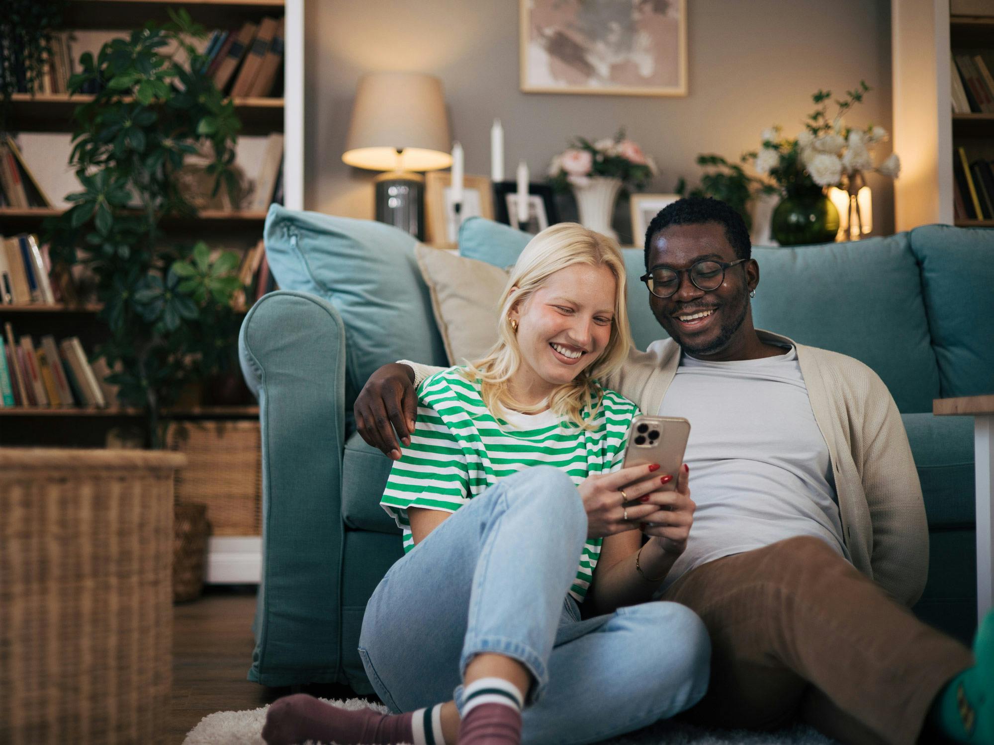 A couple sat on the floor next to their sofa researching solar panel installation on a mobile phone.