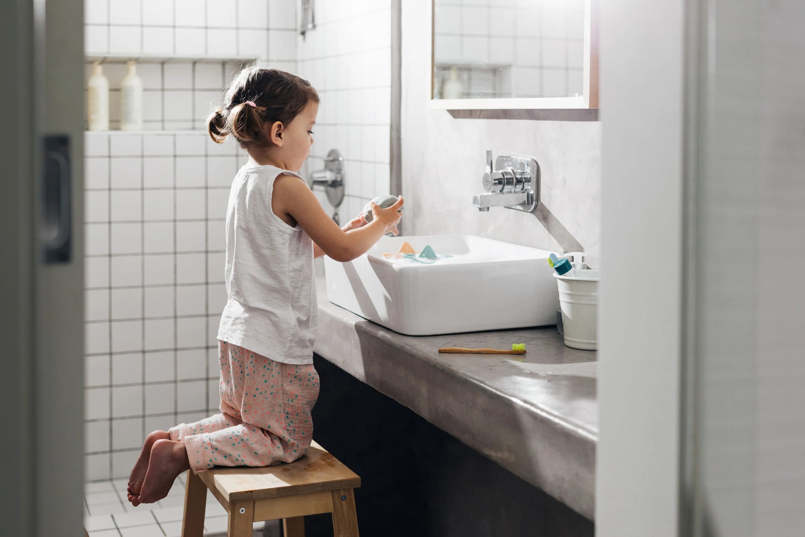 Young girl kneeling on a stool while washing her hands in the sink