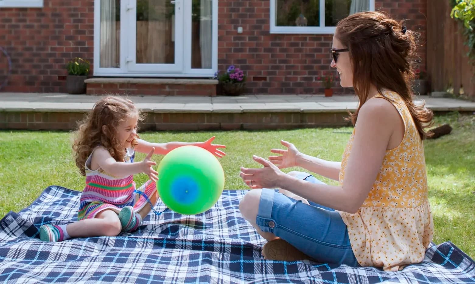 Woman & child sat in the garden playing with a ball, enjoying the sun & perks of their home solar kit from Utilita Home.
