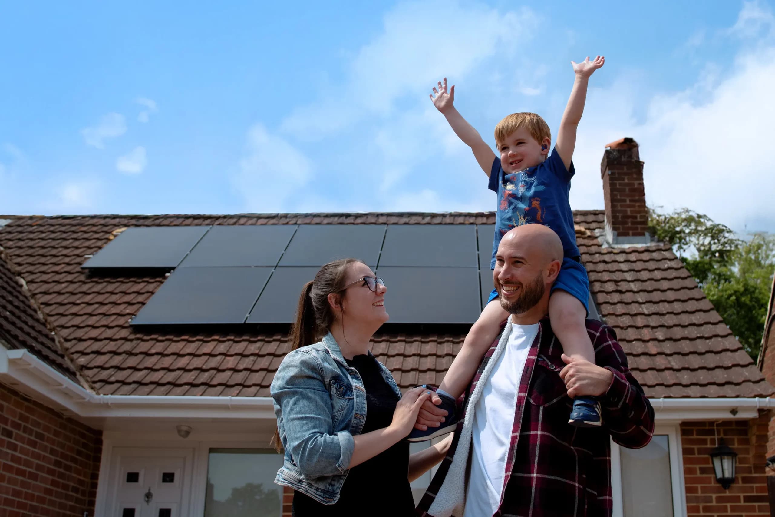 A mother & father with their son in front of a property smiling after Utilita Home installed solar panels on their UK home.