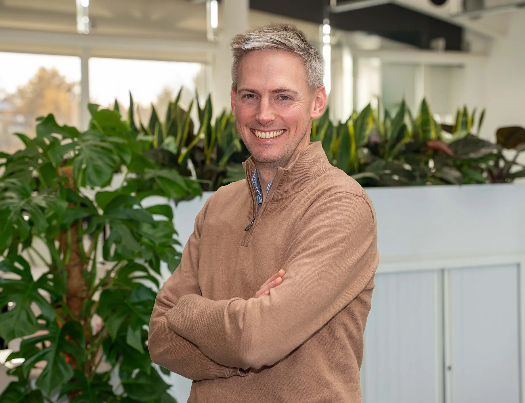 Photo of George Walters, Utilita Home's Chief Home Services Officer, with arms crossed & green plants in the background.