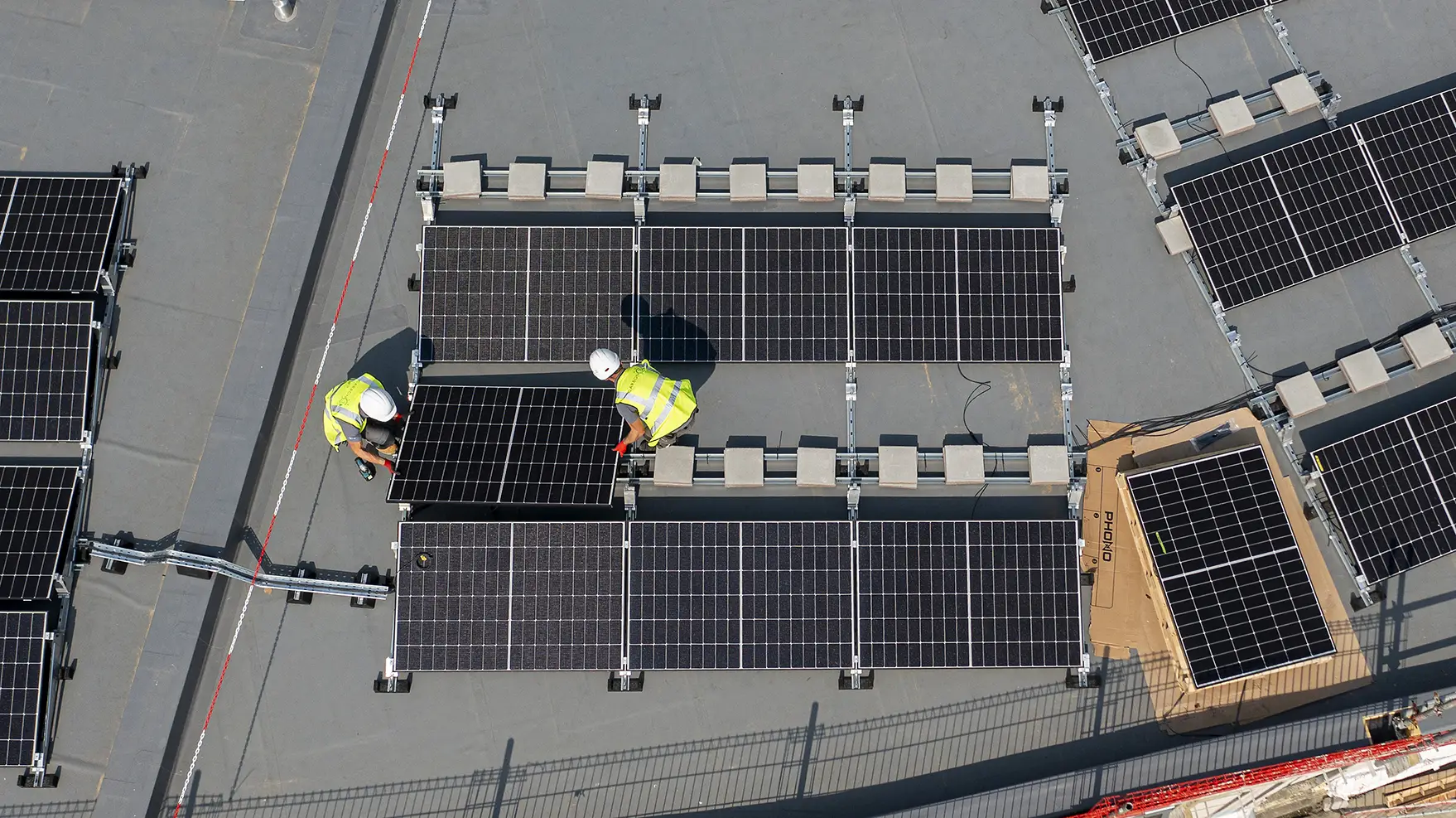Aerial view showing two engineers installing Utilita solar panels on a business's roof, helping them future-proof with solar savings.