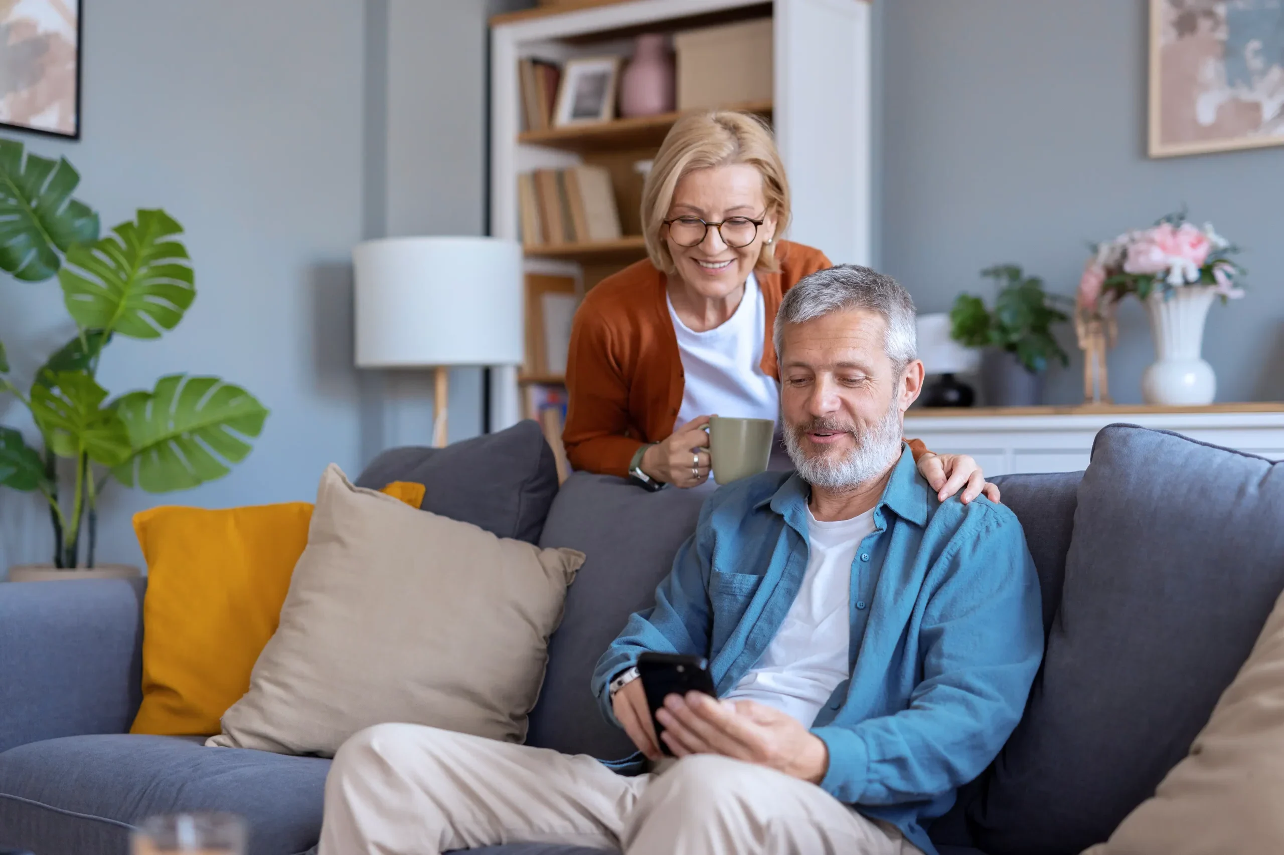Man sitting on the sofa with his wife standing behind him, getting a Utilita Home quote for solar panels & battery storage.