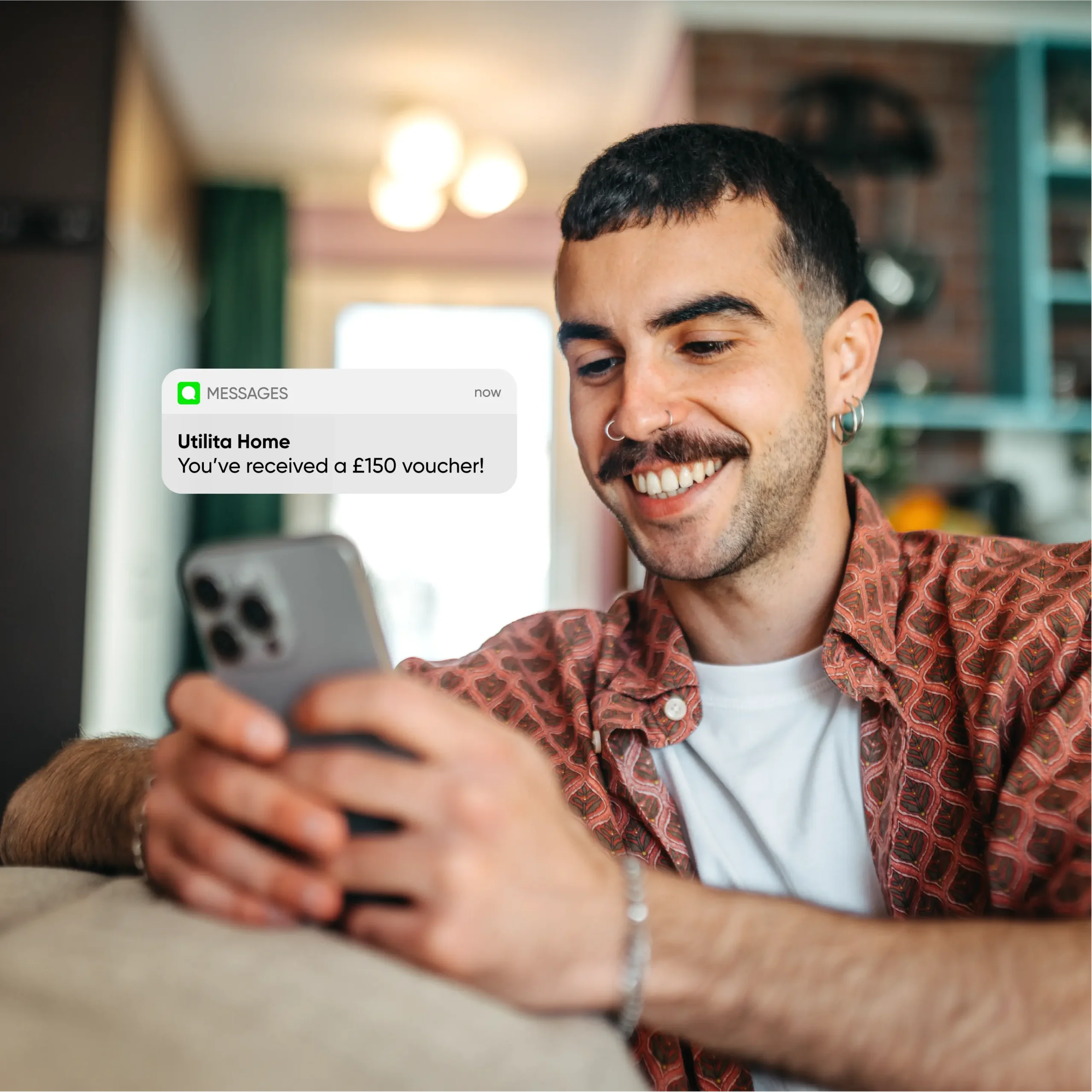 Man smiling at his phone after getting a text with a £150 voucher for referring a friend to solar from Utilita Home.